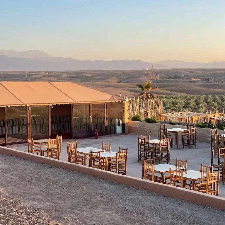 Kal Tenere Agafay outdoor seating area with wooden tables and chairs on a desert terrace overlooking distant mountains and arid landscape