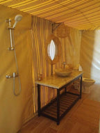 Kalimba Luxury Desert Camp bathroom with beige canvas walls, striped fabric accents, stone sink on granite countertop, wicker mirror, and shower