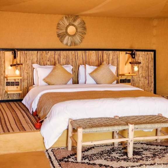 Kalimba Luxury Desert Camp bedroom with natural woven headboard, beige bedding, textured cushions, and rustic wooden bench