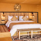 Kalimba Luxury Desert Camp bedroom with natural woven headboard, beige bedding, textured cushions, and rustic wooden bench