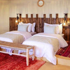 Kalimba Luxury Desert Camp bedroom with two white beds, wooden headboard, warm lighting, and red and beige rugs