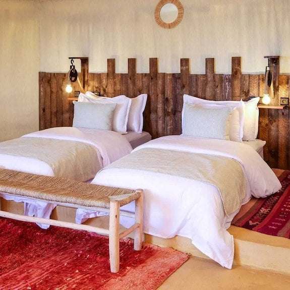 Kalimba Luxury Desert Camp bedroom with two white beds, wooden headboard, warm lighting, and red and beige rugs