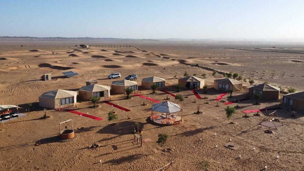 Kalimba Luxury Desert Camp with beige canvas tents arranged in a circular layout on a desert landscape with red carpets and scattered small trees