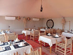 Kalimba Luxury Desert Camp dining area with wooden chairs, white tablecloths, woven seats, and rustic decor