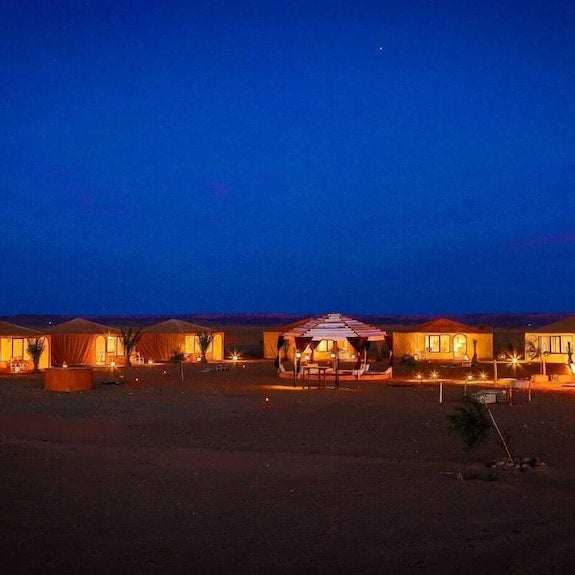 Kalimba Luxury Desert Camp illuminated desert tents with warm lights under deep blue nighttime sky in Merzouga Morocco