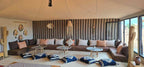 Kalimba Luxury Desert Camp indoor seating area with large brown and beige cushioned sofas, patterned wall tapestry, wooden side tables, and decorative hats and cushions