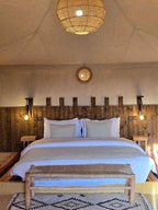 Kalimba Luxury Desert Camp interior with white bedding, wooden headboard, bedside lamps, and woven pendant light above the bed