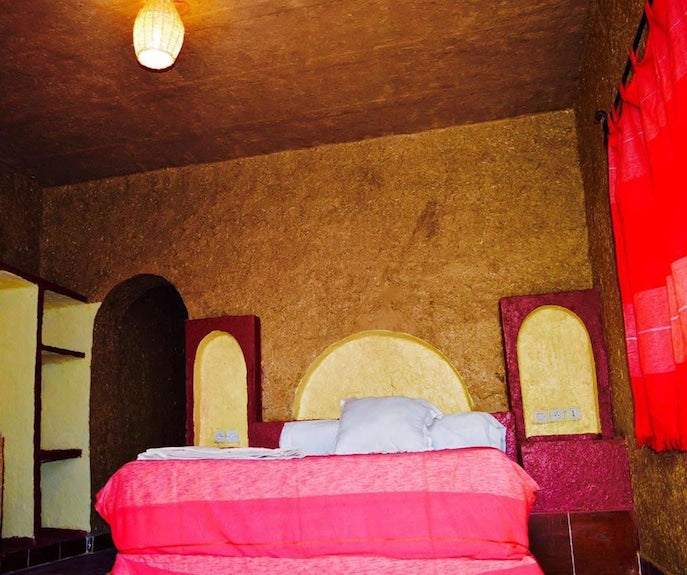 Kasbah Hotel Bar bedroom with earthy textured walls, red bedspread, white pillows, and an arched alcove design under warm lighting