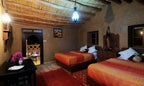 Kasbah Hotel Bar bedroom with two double beds featuring orange-red striped bedding, traditional Moroccan decor, and ambient lighting
