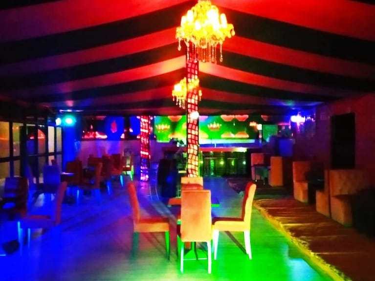 Kasbah Hotel Bar with colorful lighting, red and black striped ceiling, chandelier, wooden chairs and tables in a spacious interior