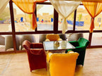 Kasbah Hotel Bar seating area with colorful velvet chairs in yellow, green, and rust around a glass table, bright curtains