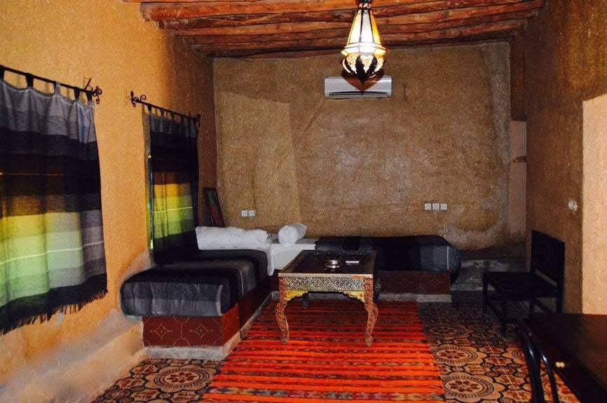 Kasbah Hotel Bar seating area with warm earthy-toned walls, wooden beams, striped curtains, patterned tiled floor, and an ornate wooden table