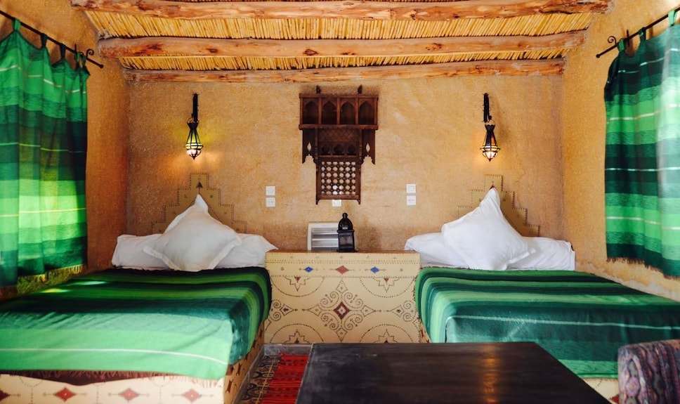 Kasbah Hotel Bar seating area with green-striped cushions, traditional beige walls, wooden ceiling beams, and Moroccan lanterns