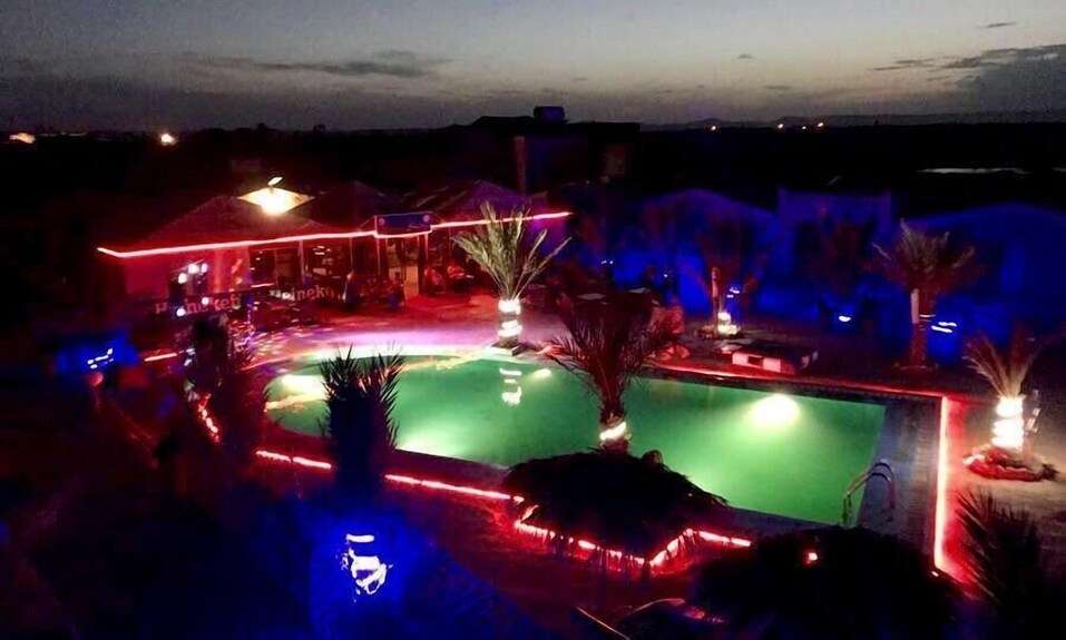 Kasbah Hotel Bar illuminated by red and blue neon lights surrounding a green-lit outdoor pool with palm trees at night