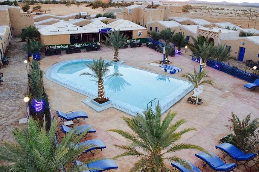 Kasbah Hotel Bar with beige adobe-style walls and blue lounge chairs around a central swimming pool bordered by palm trees
