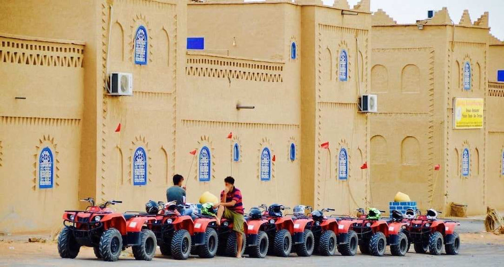 Kasbah Hotel Bar with beige traditional mud-brick architecture and a row of red all-terrain vehicles lined up outside