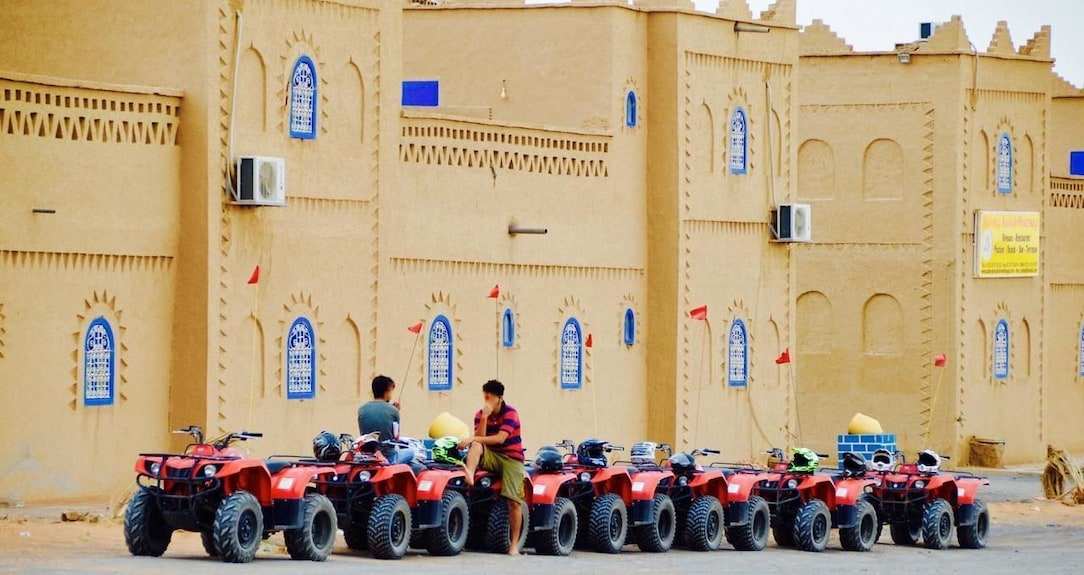 Kasbah Hotel Bar with beige traditional mud-brick architecture and a row of red all-terrain vehicles lined up outside