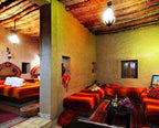 Kasbah Hotel Bar lounge area with traditional Moroccan decor featuring red and orange patterned fabrics, clay walls, and wooden ceiling beams