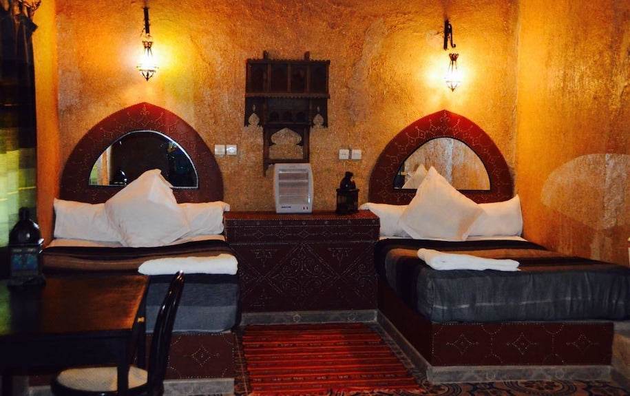 Kasbah Hotel Bar seating area with traditional Moroccan decor, warm ochre walls, arched mirrors, cushions, and ambient lighting