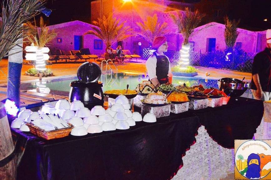Kasbah Hotel Bar outdoor buffet setup at night with illuminated palm trees, stacked white bowls, and a server in traditional attire