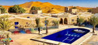 Kasbah Hotel Bar outdoor pool area with blue water, sandy beige walls, palm trees, and golden desert dunes in background