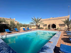 Kasbah Hotel Bar outdoor pool area in Merzouga with blue lounge chairs, palm trees, and traditional Moroccan-style beige building