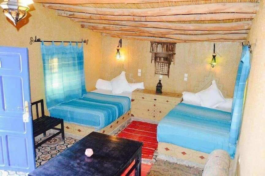 Kasbah Hotel Bar styled room with two blue striped mattresses, beige textured walls, wooden ceiling beams, and Moroccan rugs