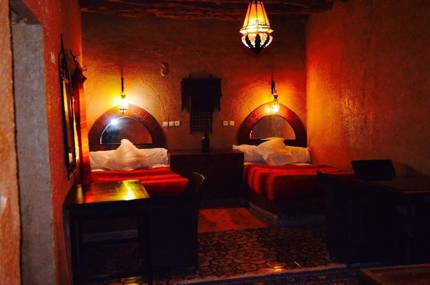Kasbah Hotel Bar seating area with warm orange clay walls, red bedding, traditional lamps, and patterned rug in Morocco