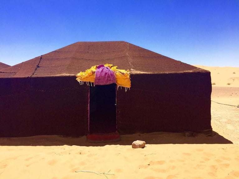 Kasbah Hotel Bar styled traditional brown fabric tent with decorative yellow and purple entrance in the desert sand under clear blue sky