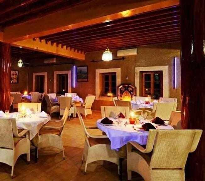 Kasbah Hotel Bar with warm lighting, traditional wooden beams, wicker chairs, white tablecloths, and cozy desert decor
