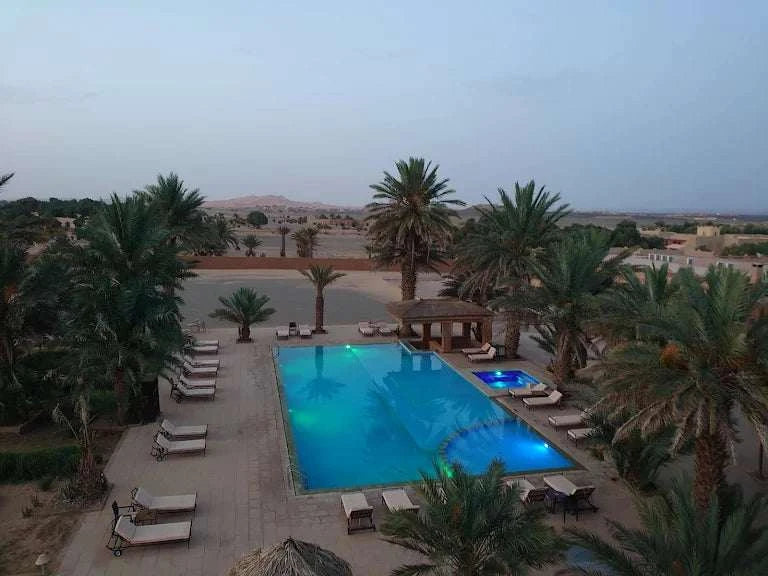 Kasbah Hotel Tombouctou outdoor rectangular pool at dusk with surrounding palm trees and lounge chairs in desert setting