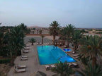 Kasbah Hotel Tombouctou outdoor rectangular pool at dusk with surrounding palm trees and lounge chairs in desert setting