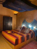 Kasbah Hotel Tombouctou bedroom with warm orange and red striped bedding, traditional blue painted headboard, and rustic wood wardrobe
