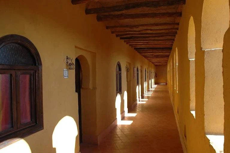Kasbah Hotel Tombouctou long corridor with warm yellow walls, arched windows, wooden beams, and terracotta floor tiles