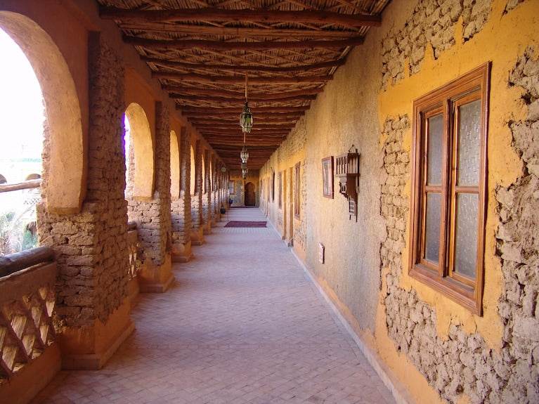Kasbah Hotel Xaluca corridor with adobe walls, yellow plaster, stone details, wooden framed windows and rustic ceiling beams