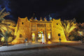 Kasbah Hotel Xaluca adobe building with illuminated entrance, traditional Moroccan architecture, and decorative figures on roof at night