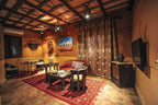 Kasbah Hotel Xaluca living room with warm adobe walls, rustic wood ceiling, patterned red rug, and wicker furniture with cushions