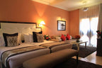 Kasbah Hotel Xaluca cozy hotel room with twin beds, beige and brown patterned cushions, coral walls, and bright window light