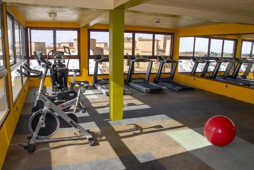 Kasbah Hotel Xaluca gym with yellow walls, large windows, several treadmills, exercise bikes, and a red exercise ball