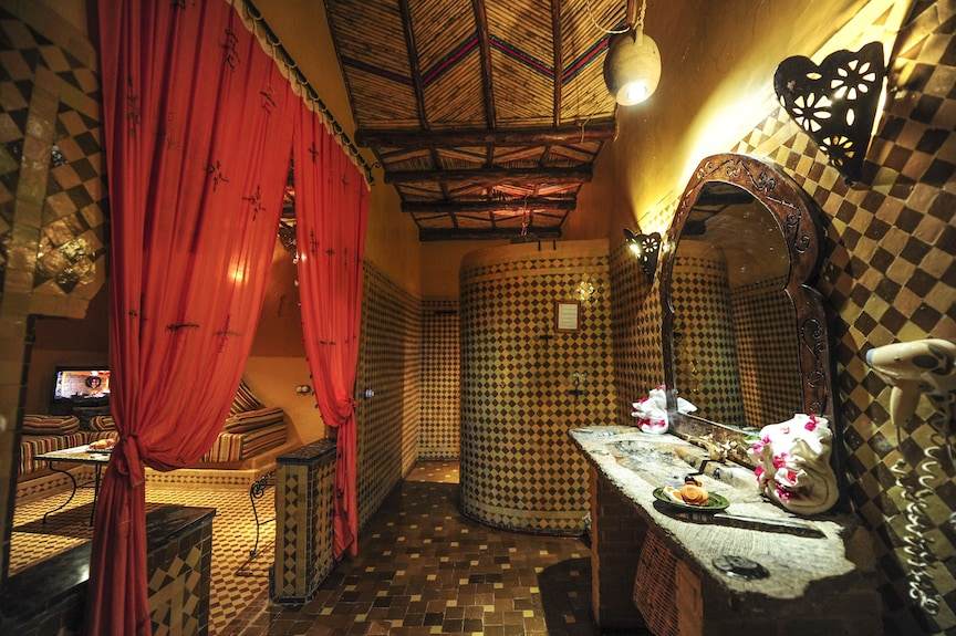 Kasbah Hotel Xaluca Moroccan style bathroom with mosaic tiled walls and floor, wooden framed mirror, and red curtains