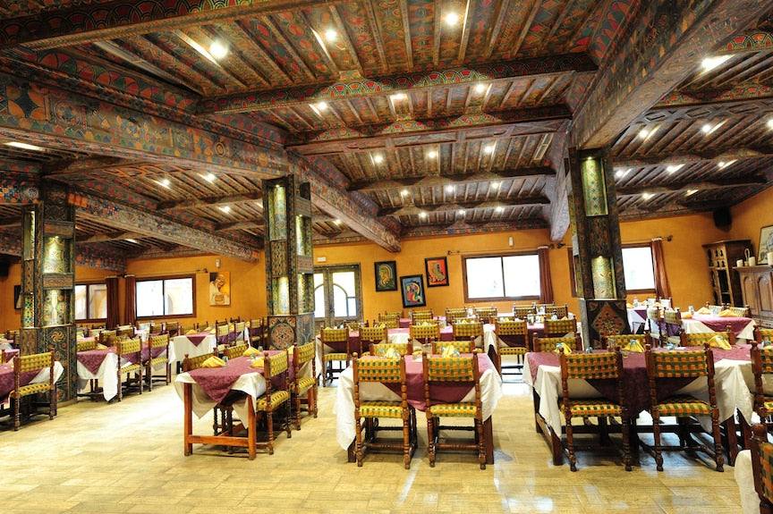 Kasbah Hotel Xaluca spacious dining room with traditional Moroccan wooden ceiling beams and colorful patterned chairs