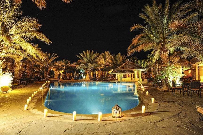 Kasbah Hotel Xaluca nighttime outdoor pool surrounded by lit candles and palm trees in a desert oasis setting