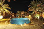 Kasbah Hotel Xaluca nighttime outdoor pool surrounded by lit candles and palm trees in a desert oasis setting