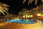 Kasbah Hotel Xaluca outdoor swimming pool at night with lit candles, palm trees, and adobe-style buildings