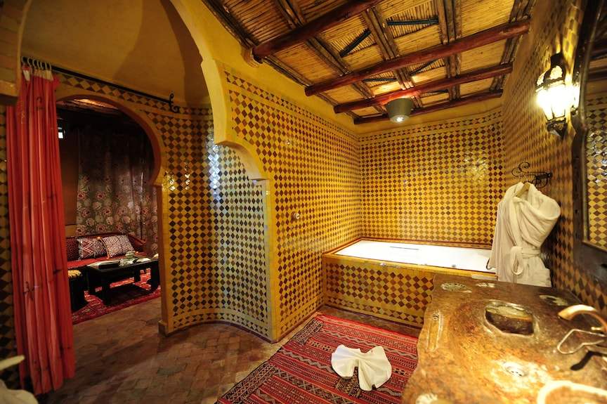 Kasbah Hotel Xaluca bathroom with yellow geometric patterned tiles, wooden ceiling, stone sink, and white robe hung on wall