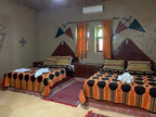 Kasbah Le Touareg bedroom with two double beds featuring orange, black, and brown geometric patterned bedspreads and traditional wall murals