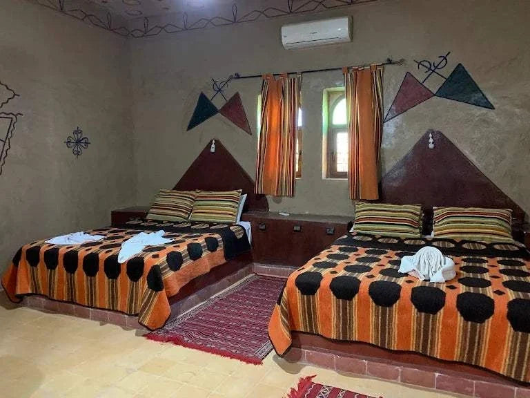 Kasbah Le Touareg bedroom with two double beds featuring orange, black, and brown geometric patterned bedspreads and traditional wall murals