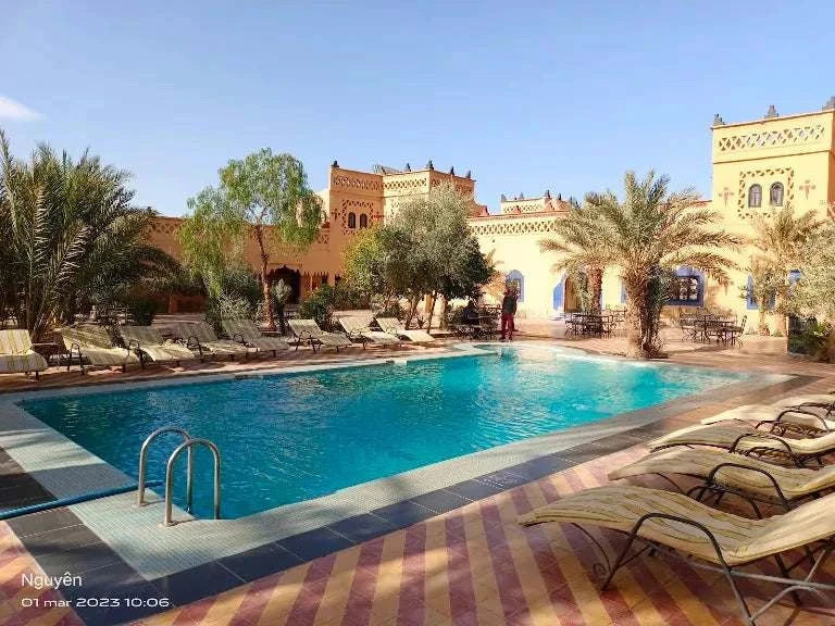 Kasbah Le Touareg outdoor swimming pool with turquoise water, surrounded by beige loungers, palm trees, and traditional Moroccan architecture