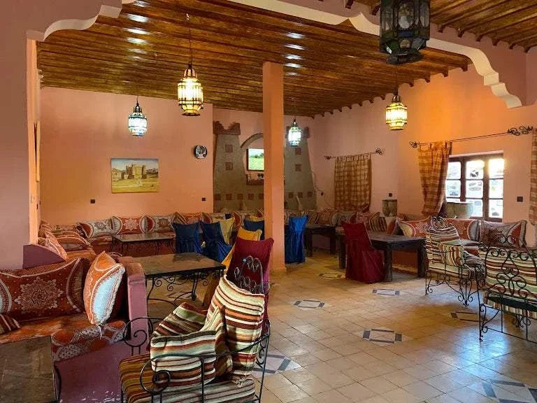 Interior lounge of Kasbah Le Touareg featuring warm peach walls, traditional Moroccan patterned cushions, wooden beam ceiling, and ornate lanterns