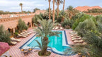 Kasbah Le Touareg outdoor swimming pool surrounded by palm trees, terracotta walls, and sun loungers in Merzouga Morocco